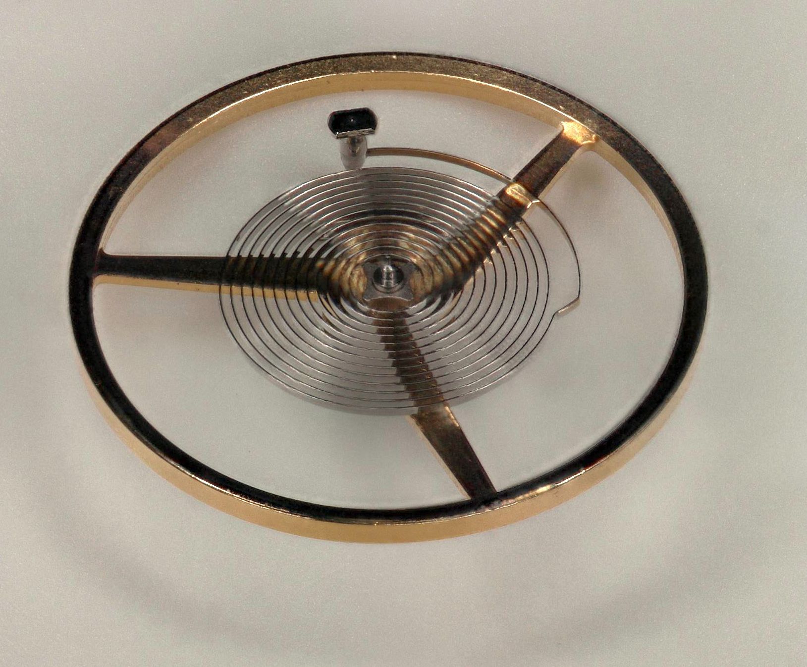 A watch balance wheel and its hairspring photographed out of the movement against a plain ground, the flat spiral of the spring and the spacing between its coils clearly visible.