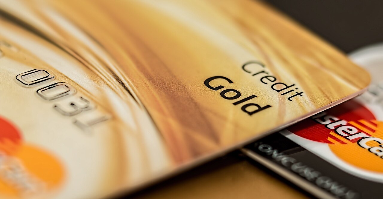 Several credit cards lying spread and overlapping on a dark surface, shot at a shallow depth of field. A gold card reading "Credit Gold" sits in front, a MasterCard shows its red and orange circles behind it, and a third dark card is stacked behind that.