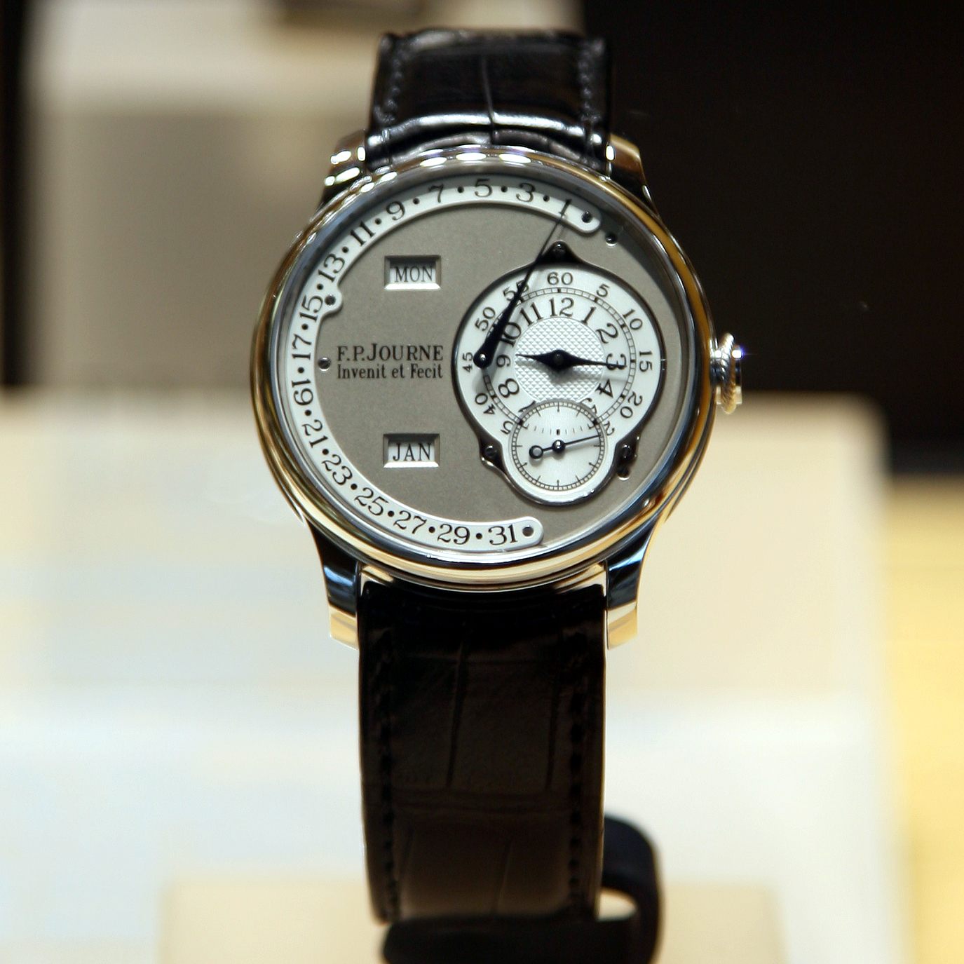 An F.P. Journe wristwatch in a steel case, photographed straight-on. The dial is signed "F.P.Journe Invenit et Fecit," with day and month display windows, a date scale running around the outer edge, and two small subdials below the centre for the running seconds and a secondary indication.