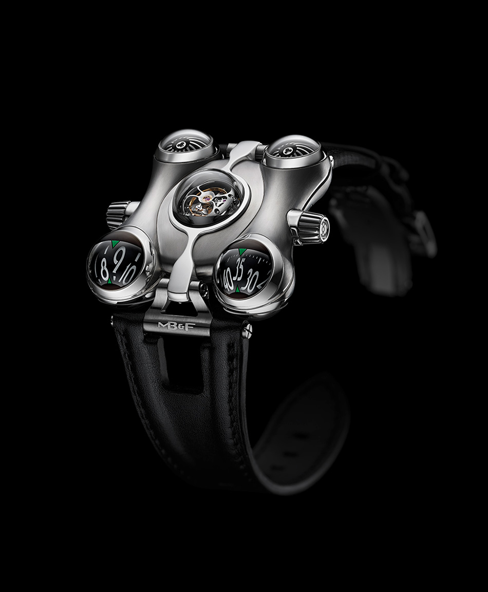 An MB&F Horological Machine No.6 in titanium against black: a curved biomorphic case with two spherical time indicators at the front, a domed sapphire over the flying tourbillon at the centre, and turbine domes at the rear, on a black leather strap.