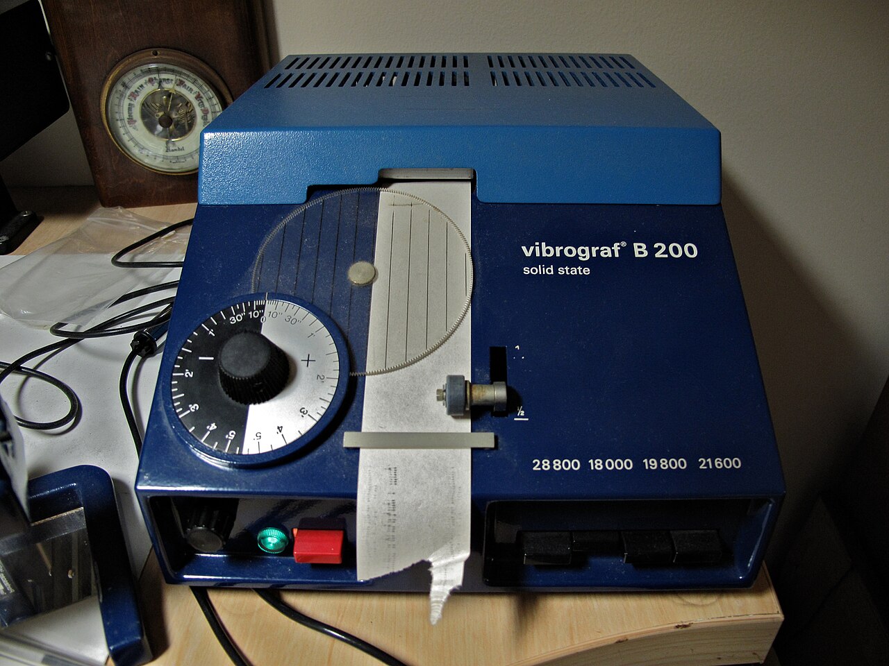 A Vibrograf B200 watch timing machine on a bench, its dial controls and microphone clamp in view, of the kind used to measure a movement's daily rate.
